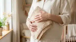 אישה בחולצת כותנה אוחזת שמיכת תינוק סרוגה, ביטוי לתכנון משפחה והנקה אחרי הקטנת חזה